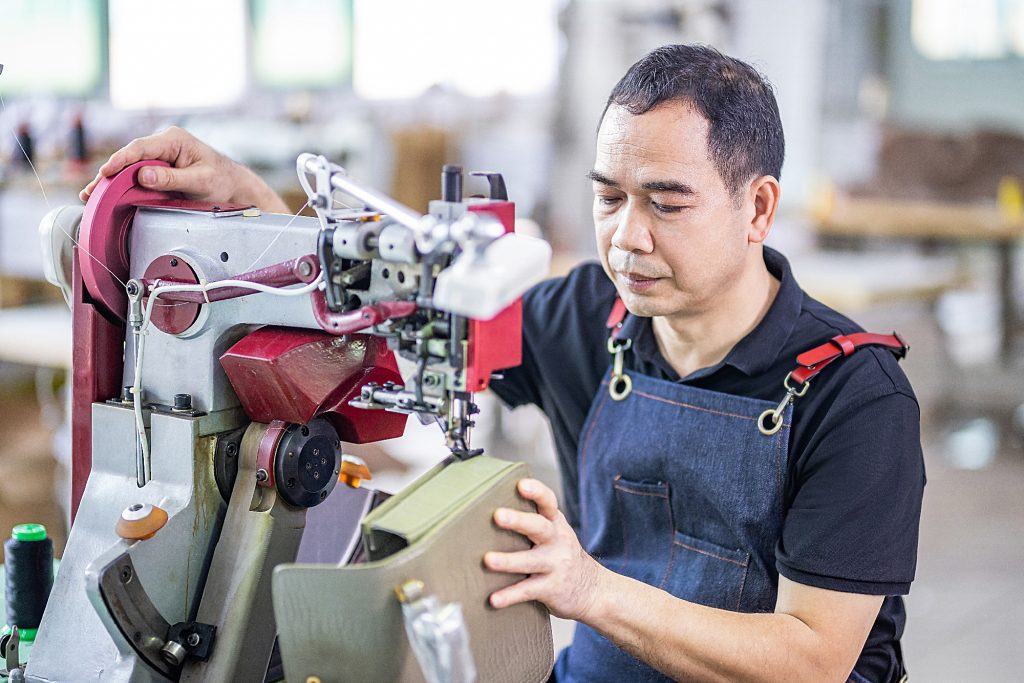 Skilled worker making handbag samples and checking stitching quality during OEM and ODM production